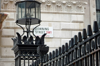 A tight cropped view of some railings and the side of a building. A sign reads: Downing Street SW1.