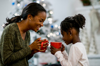 Mother and child holding mugs, sat in front of a Christmas tree