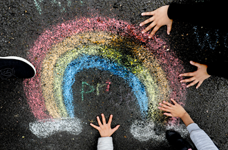 Rainbow drawn on a school playground in chalk with children's hands around it