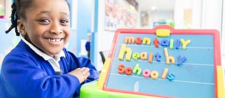 Child smiling - board with 'Mentally Healthy Schools' on it