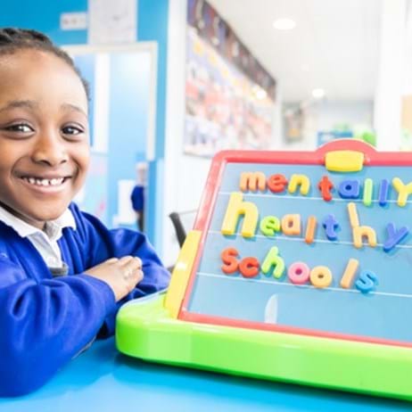 School girl with board spelling out Mentally Healthy Schools