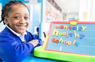 Girl smiling next to magnetic board that says Mentally Healthy Schools