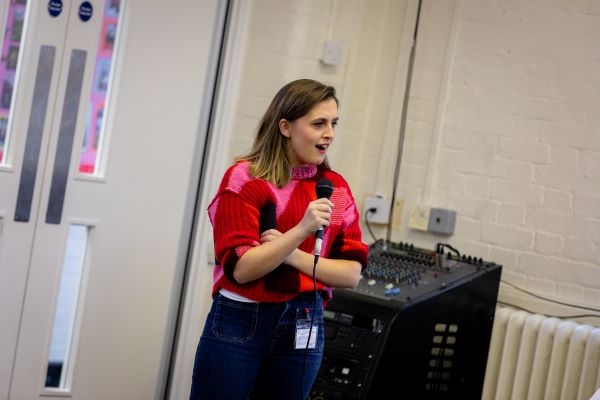 Kia Pegg presenting the BAFTA Roadshow to pupils at Heathland Primary School. She is holding a microphone and is looking away from the camera.