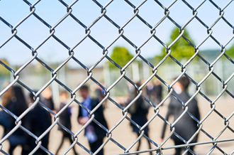 Secondary aged students in playground, out of focus, behind a wire fence