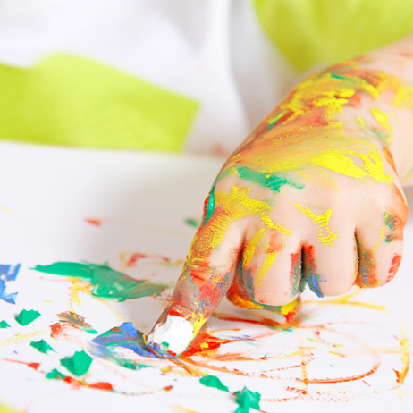 Child's hand covered in paint, finger painting on piece of paper