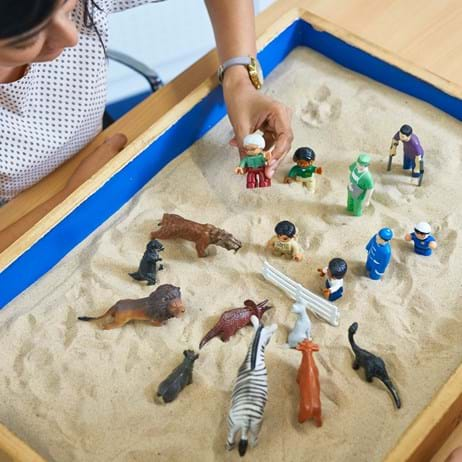 Adults playing with toys in a stand tray for counselling training