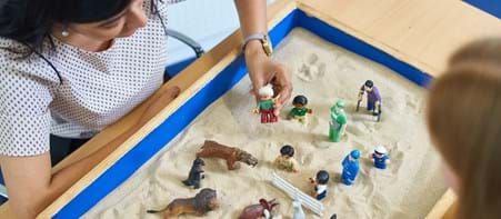 Two people using sand tray with toys in it