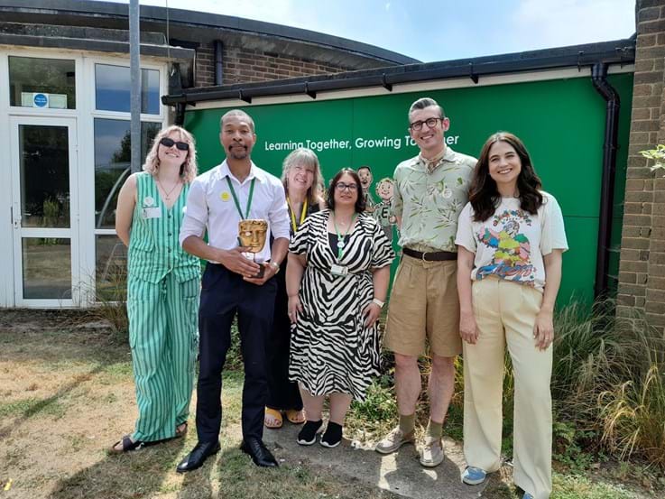 Teachers and talents holding a BAFTA award outside school grounds