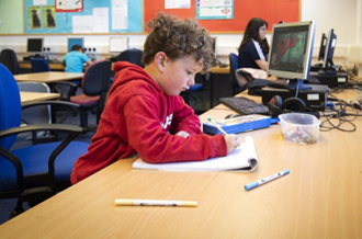 Boy in red hoodie sits at desk writing in a notepad