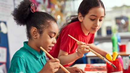 Two young girls sitting at a table, painting pictures