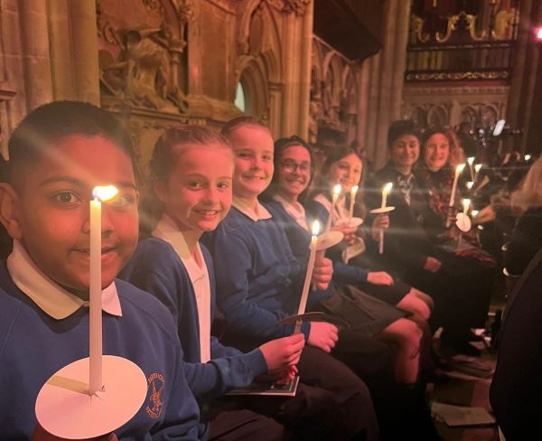 St John's Primary School pupils holding a candle in Westminster Abbey. The children are looking into the camera and smiling.