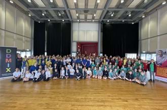 Pupils from lots of primary schools standing in rows and smiling at the camera after their DDMIX workshop with Dame Darcey Bussell DBE