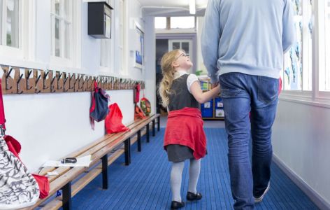 A primary aged girl holding hands with her parent and walking in a school corridor