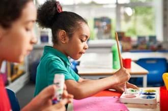 young girl sitting at a table in a classroom and painting