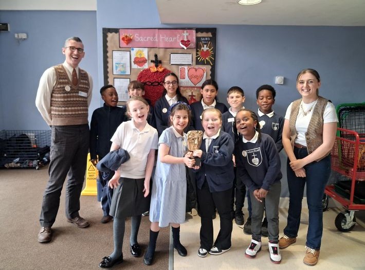 Kia Pegg and Ben Shires with pupils from Sacred Heart Primary School, all smiling at the camera.
