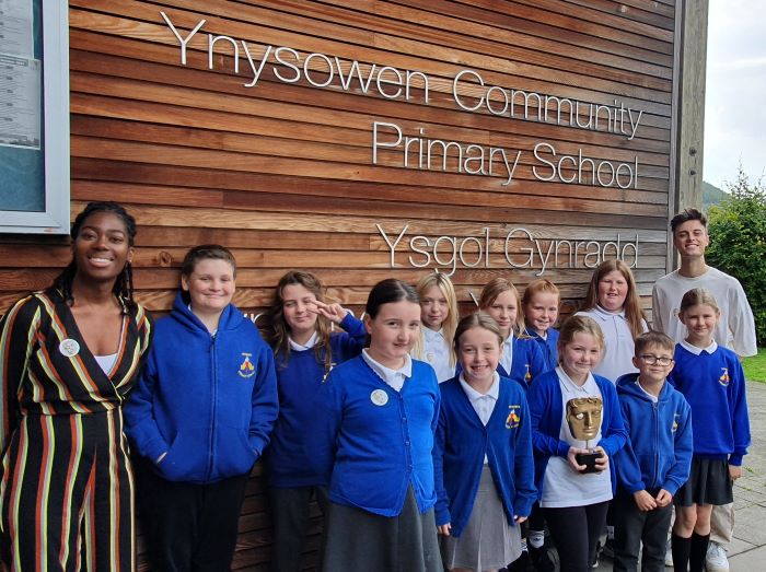 Pupils at Ynysowen Primary School posing for a photo with TV presenters Shanequa Paris (left) and Joe Tasker (right). The middle child in the first row is holding a BAFTA trophy.