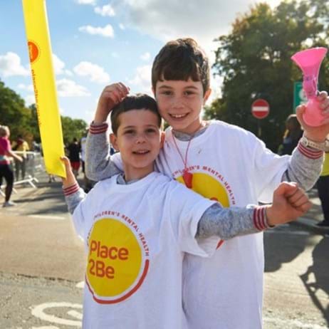 two children wearing Place2Be t-shirts cheering on marathon runners