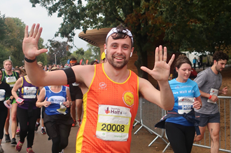 A runner wearing the Place2Be running vest raising two hands to camera