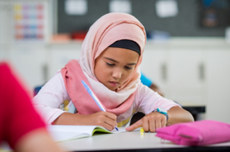 Young girl wearing hijab, writing on desk at school