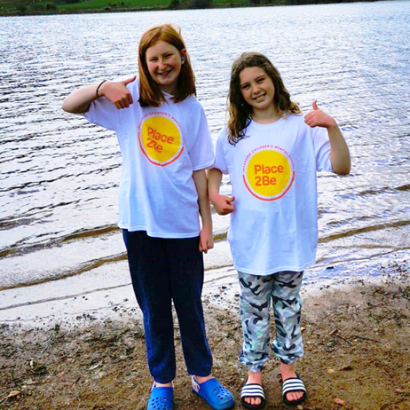 Two girls standing by a lake with thumbs up
