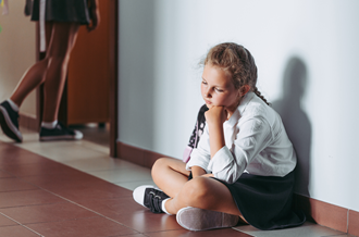 Girl in school uniform sat in corridor looking pensive