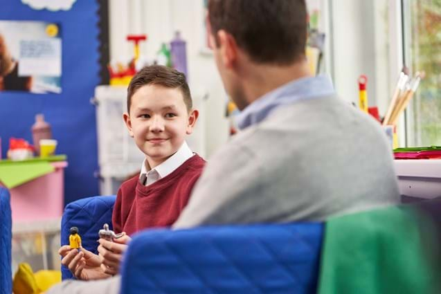 Boy sitting on sofa and playing with toys talking to counsellor