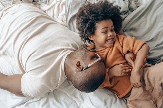 Father and child lying down, father pretending to be asleep