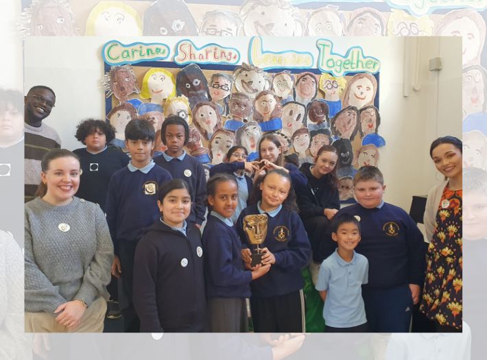 De-Graft Mensah and Mirain Iwerydd standing in a classroom with smiling Tredegarville C.I.W. Primary School students. De-Graft Mensah and Mirain Iwerydd standing in a classroom with smiling Tredegarville C.I.W. Primary School students.