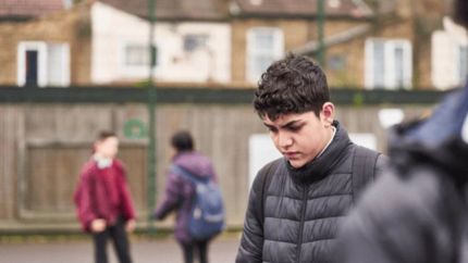 School pupil standing on the playground looking at the ground
