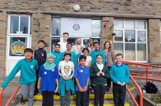 Pupils with presenters Joe Tasker and Shanequa Paris smiling at the camera. One pupil is holding the BAFTA Trophy.