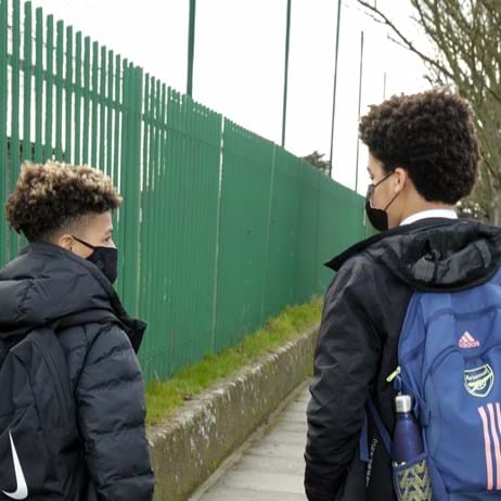 two boys with masks and backpack outside of school