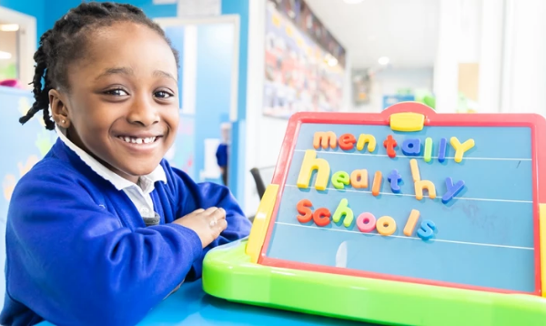 Girl smiling next to magnetic board that says Mentally Healthy Schools