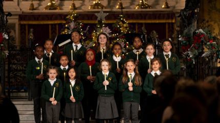 The Goldfinch Primary School choir performing at Holy Trinity Church in Sloane Square. Fifteen children dressed in school uniform are holding candles while singing.