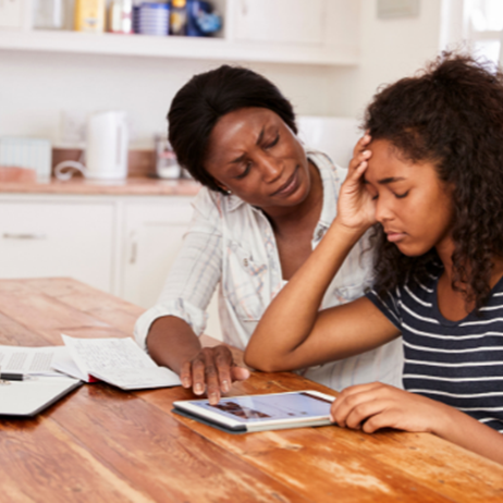 A parent sitting and comforting her daughter who is upset whilst they sit at the kitchen table looking at school work