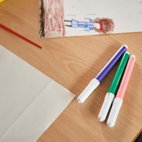 Paper, paint brush, drawing and pens on a table in classroom