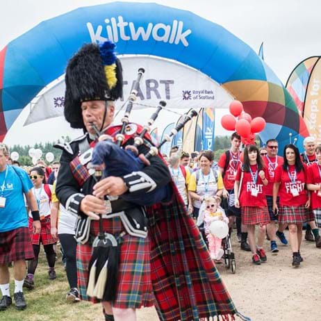Man playing bagpipes walking under Kiltwalk archway
