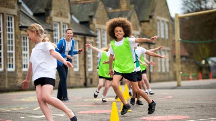 Children running in playground, one child in a green vest smiling at camera