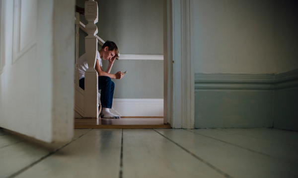 Teenage boy sat on stairs with head in hand, looking at mobile phone