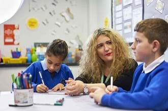 school staff with two primary school pupils, sitting at a desk in a classroom