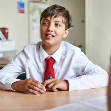 Secondary school boy sitting at a classroom table looking at teacher