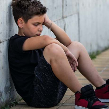 Boy sitting against a wall looking sad