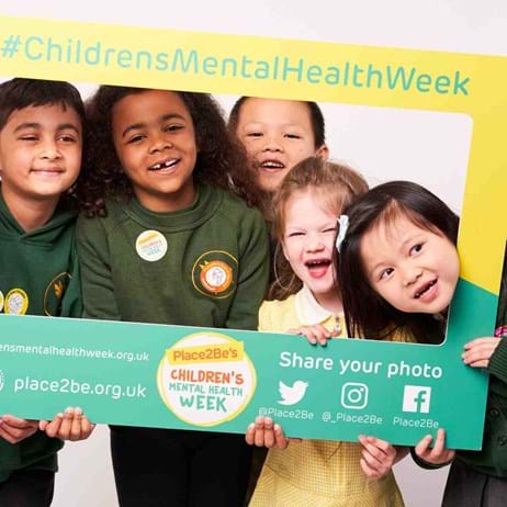 five young children standing in a Children's Mental Health Week selfie frame, laughing and smiling at the camera
