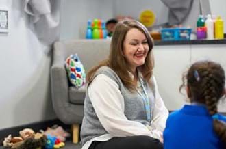 Female counsellor sat on the floor with a child laughing and smiling