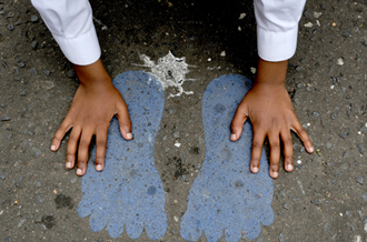Child placing their hands on playground, which has a chalk drawing of two footprints