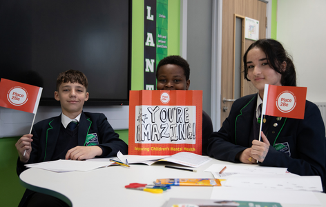 Secondary school children waving Place2Be flags and a sign that reads "You're amazing"