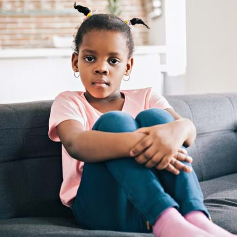 Girl on sofa holding her knees looking upset