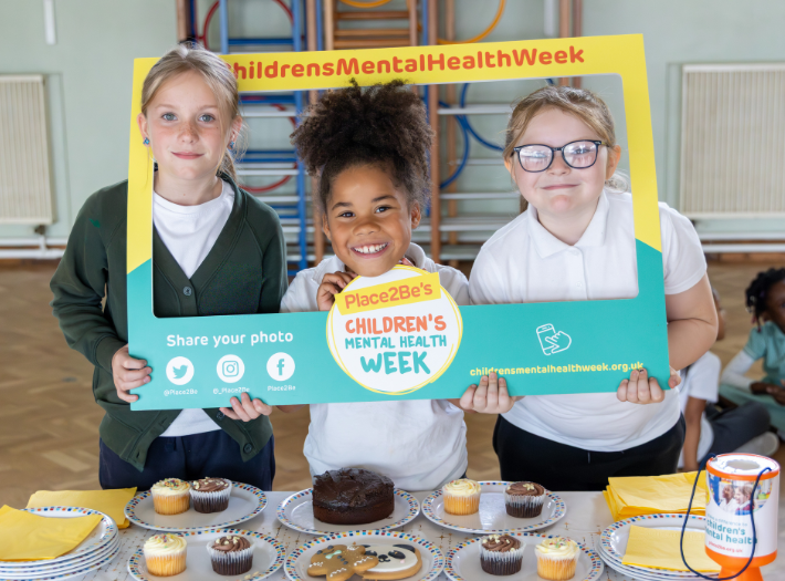 Children hosting a bake sale holding a Place2Be branded frame