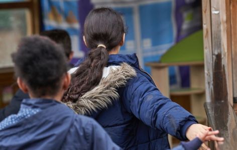 Two children wearing coats outside in school playground