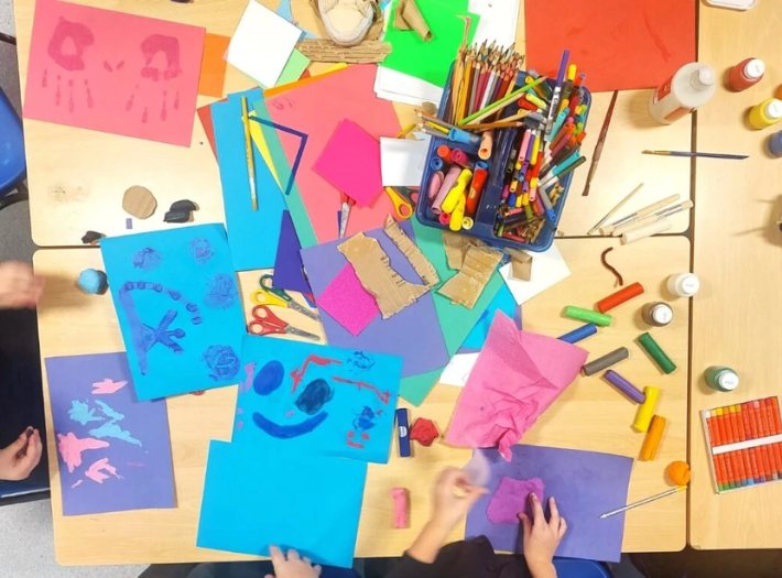 bird's-eye view of classroom table covered in colourful arts supplies
