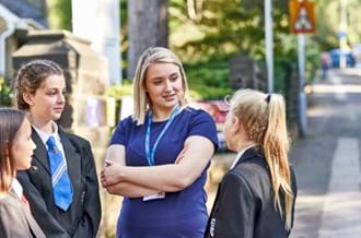 Female teacher speaks to 3 female pupils outside school gates